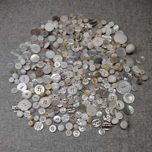 Lote de botões vintage variados, em sua maioria brancos, diversos conjuntos combinando, incluindo botões de madrepérola e de plástico.