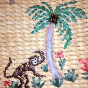 May include: Woven straw handbag with an embroidered tropical scene. The design features a monkey, palm tree, and flowers in shades of brown, green, pink, and purple. The word "SCALA" is on a small metal tag.