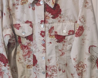 May include: A cream-coloured denim jacket with a floral print featuring red, pink, and yellow flowers. The jacket has a button closure and two front pockets.