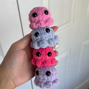 Op de afbeelding: Een stapel van vier gehaakte octopus knuffels in tinten roze, paars en blauw. Elke octopus heeft zwarte knoopjesogen.