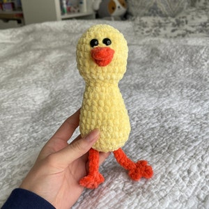 May include: A yellow crocheted chick toy with black eyes and an orange beak. The chick has orange crocheted legs.