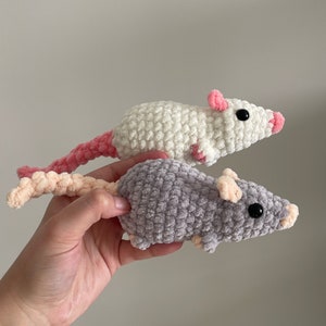 May include: Two crocheted rat toys. One is white with pink ears and tail, the other is gray with pink ears and tail.
