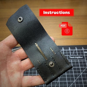 May include: A black leather needle case featuring a snap button closure and two internal slots holding gold-colored needles. The case includes a red rectangular graphic with the text Instructions and a red PDF download icon.