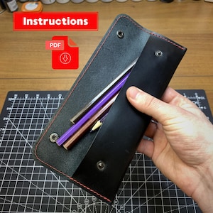 May include: Black leather pencil case with red stitching, holding several colored pencils. The case is open, revealing the pencils inside. The word "Instructions" is displayed in a red rectangle.
