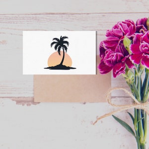 May include: A white card with a black silhouette of a palm tree on a small island with a pink and orange sunset behind it. The card is sitting on a brown envelope.