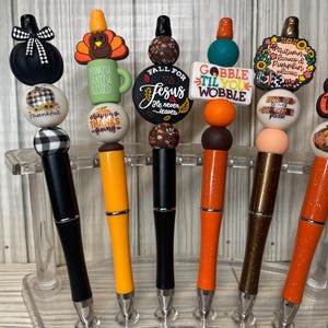 May include: Six pens featuring decorative toppers with autumn themes. The toppers include pumpkins, a turkey, and text such as 'Fall for Jesus', 'Gobble til you wobble', 'Autumn leaves & pumpkin please', and 'Grateful Thankful Blessed' in various colors.