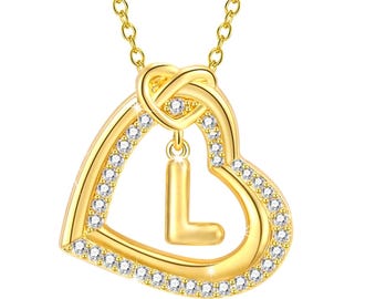 Puede incluir: Collar dorado con un colgante de doble corazón con un borde brillante de pequeños cristales transparentes. El colgante tiene una letra "L" colgante en el centro. La cadena del collar también es dorada y tiene un diseño delicado.