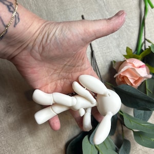 May include: A white articulated doll shaped like a rabbit with long ears. The doll is posed with its arms outstretched and its legs bent.