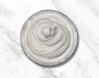 May include: A small glass bowl filled with a white, creamy substance, possibly whipped cream or frosting. The bowl is sitting on a white marble surface.