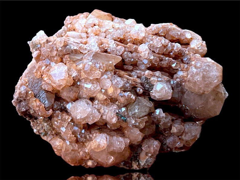 May include: A cluster of pink and brown crystals with a rough, natural texture. The crystals are densely packed together, creating a visually interesting and unique piece.