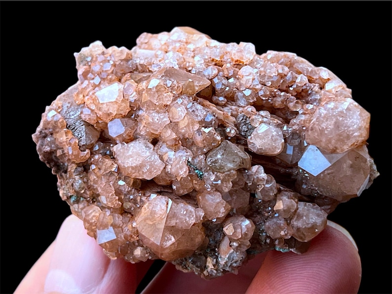 May include: A cluster of small, translucent, orange-brown crystals on a matrix of dark brown rock. The crystals have a rough, faceted texture and are arranged in a dense, irregular pattern.