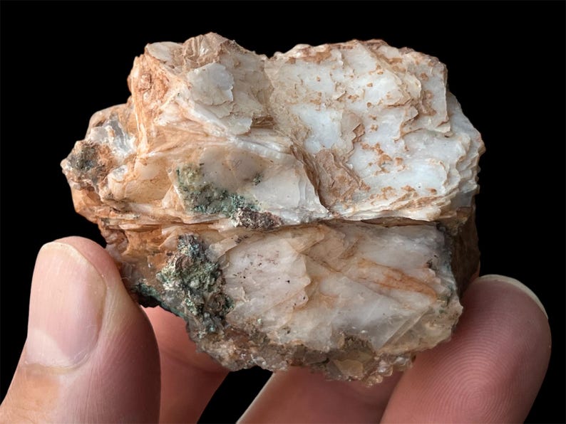 May include: A rough, white and brown rock with a layered, flaky texture. The rock has a green mineral deposit on one side.