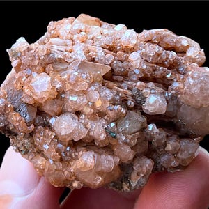 May include: A cluster of small, clear quartz crystals with a reddish-brown hue. The crystals are densely packed together, forming a rough, irregular shape. The quartz crystals are translucent and have a glassy luster.
