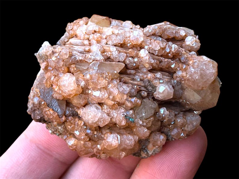 May include: A cluster of light brown and clear quartz crystals on a matrix of brown and gray rock. The crystals are clustered together in a dense formation, with some of the crystals having a more pointed shape than others.