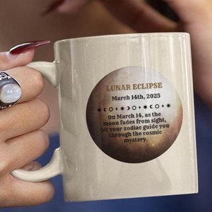 Puede incluir: Taza de cerámica blanca con un diseño marrón y dorado que presenta el texto "LUNAR ECLIPSE March 14th, 2025 COOCO On March 14, as the moon fades from sight, let your zodiac guide you through the cosmic mystery."
