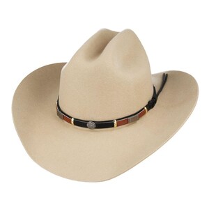 Pode incluir: Um chap&eacute;u de cowboy de feltro bege com uma faixa de couro preta e detalhes prateados. A faixa tem uma incrusta&ccedil;&atilde;o de couro marrom e detalhes dourados.