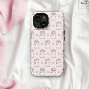 May include: A white phone case with a pink background and a repeating pattern of gray hamsters wearing pink bows. The hamsters are surrounded by small pink flowers.