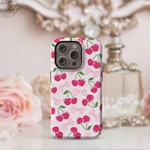Op de afbeelding: Een witte telefoonhoes met een roze en groene kersenprint. De hoes heeft een verhoogde camerabult met drie lenzen.