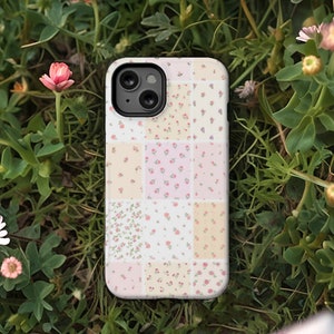 Op de afbeelding: Een witte telefoonhoes met een patchwork-ontwerp met verschillende kleine bloemenpatronen in roze, geel en wit.