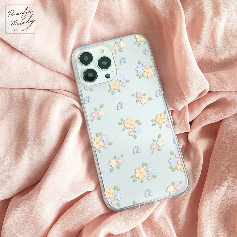 May include: A clear phone case with a light blue background and a floral pattern in shades of yellow, pink, and purple. The case is designed for an iPhone with a triple camera lens.
