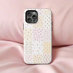 Op de afbeelding: Een witte iPhone-hoes met een patchwork-ontwerp met kleine roze en gele bloemen. De hoes heeft een zwarte camerabult met drie lenzen.