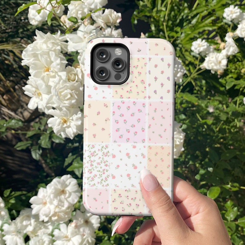 Op de afbeelding: Een witte telefoonhoes met een patchwork-ontwerp met kleine roze en gele bloemen. De hoes heeft een zwarte camerabult met drie lenzen.