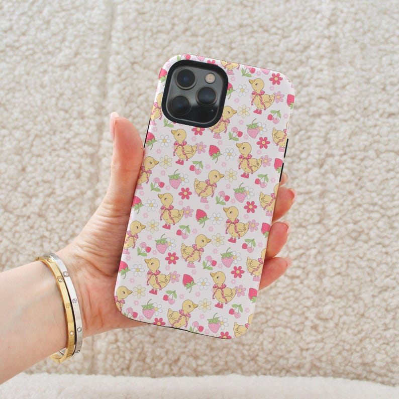 May include: A white phone case with a pattern of yellow ducklings and pink strawberries.