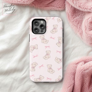 May include: A pink phone case with a repeating pattern of white teddy bears and pink bows.