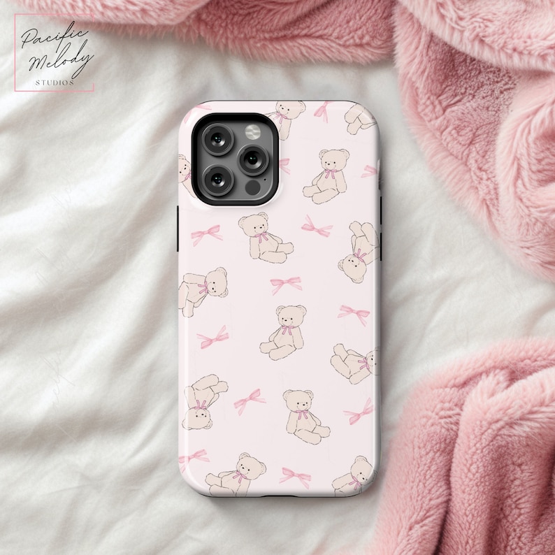 May include: A pink phone case with a repeating pattern of white teddy bears and pink bows.