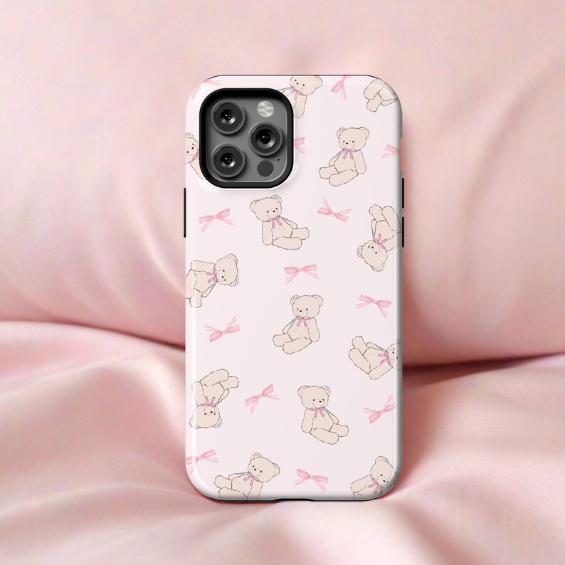 May include: A white phone case with a repeating pattern of pink bows and small teddy bears.