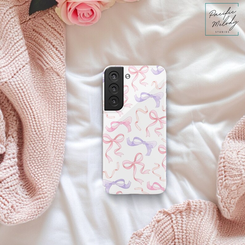 a white phone case with a pattern of randomly placed large bows through out the case. The bows are illustrated in a watercolor sketch style, and are shades of warm pink and purple
