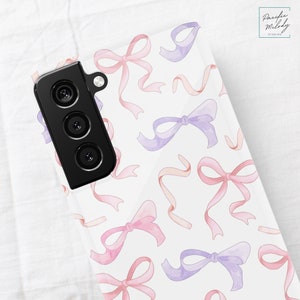 May include: A white phone case with a pattern of pink and purple watercolor bows. The case has a black camera lens cutout.