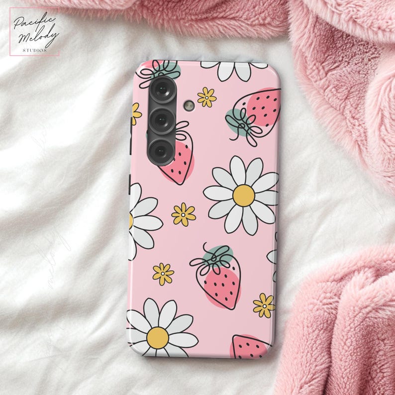 May include: A pink phone case with a pattern of white daisies, green leaves, and red strawberries. The case has a black camera lens cutout.