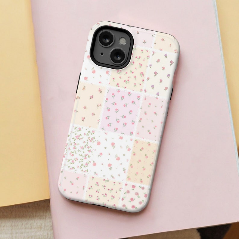 Op de afbeelding: Een witte telefoonhoes met een patchwork-ontwerp met verschillende bloemenpatronen in roze, gele en witte tinten. De hoes heeft een zwarte camera lens uitsparing.