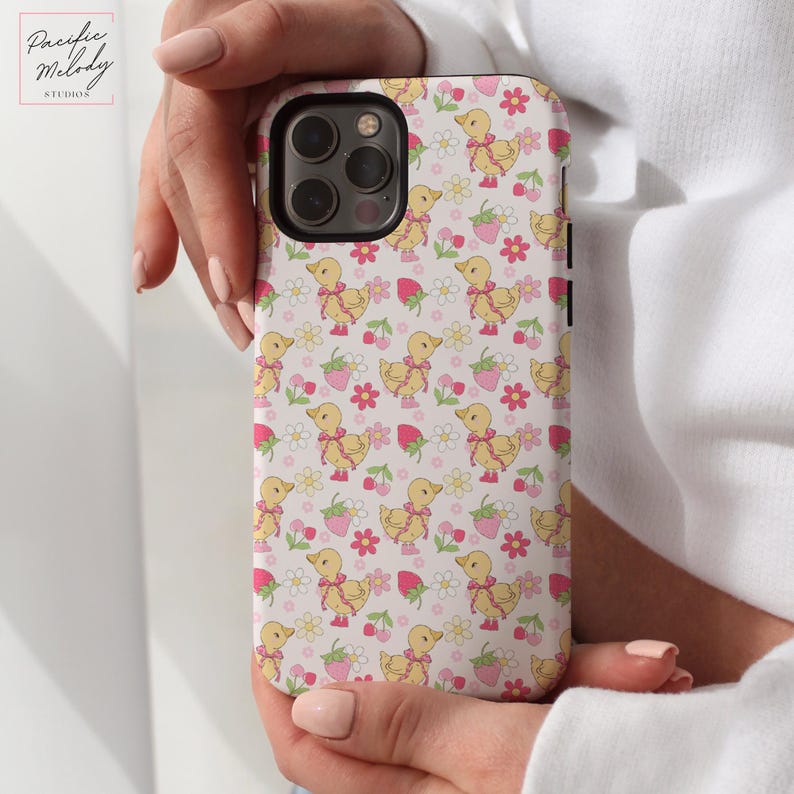 May include: A white phone case with a pattern of yellow ducklings, pink flowers, and red strawberries.