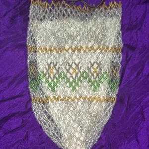 May include: A white beaded bag with a gold and green geometric pattern. The bag has a drawstring closure and a tassel.