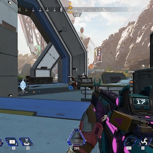 May include: A first-person view of a video game, showing a player holding a colorful gun with a pink and teal design. The game's user interface is visible, including the player's health bar, the round timer, and the number of squads remaining. The game's environment is a futuristic cityscape with a large metal structure in the background.