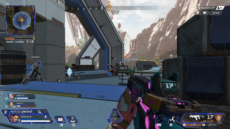 May include: A first-person view of a video game, showing a player holding a colorful gun with a pink and teal design. The game's user interface is visible, including the player's health bar, the round timer, and the number of squads remaining. The game's environment is a futuristic cityscape with a large metal structure in the background.