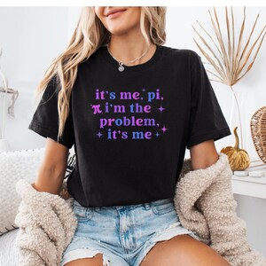 May include: Black t-shirt with the text "it's me, pi, i'm the problem, + it's me +" in pink and blue lettering.