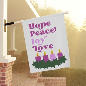 May include: A white flag with the words "Hope Peace Joy Love" in purple lettering. Four purple candles are in a green wreath at the bottom of the flag.