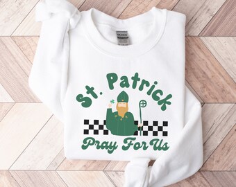May include: White sweatshirt with a green and black graphic of a cartoon St. Patrick holding a shamrock and a staff. The text "St. Patrick Pray For Us" is printed in green.