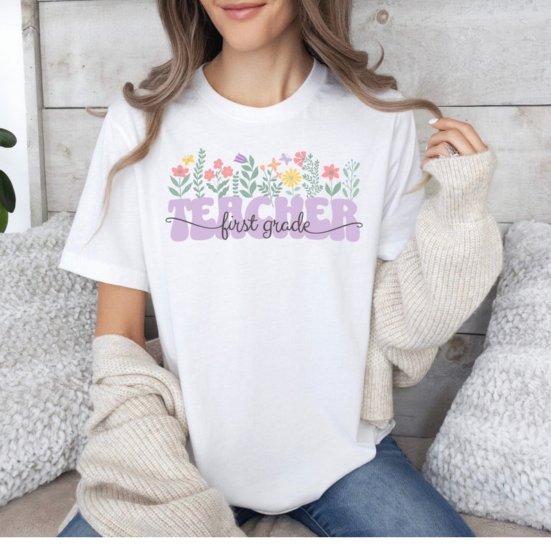May include: White t-shirt with a purple "Teacher first grade" graphic with floral accents.