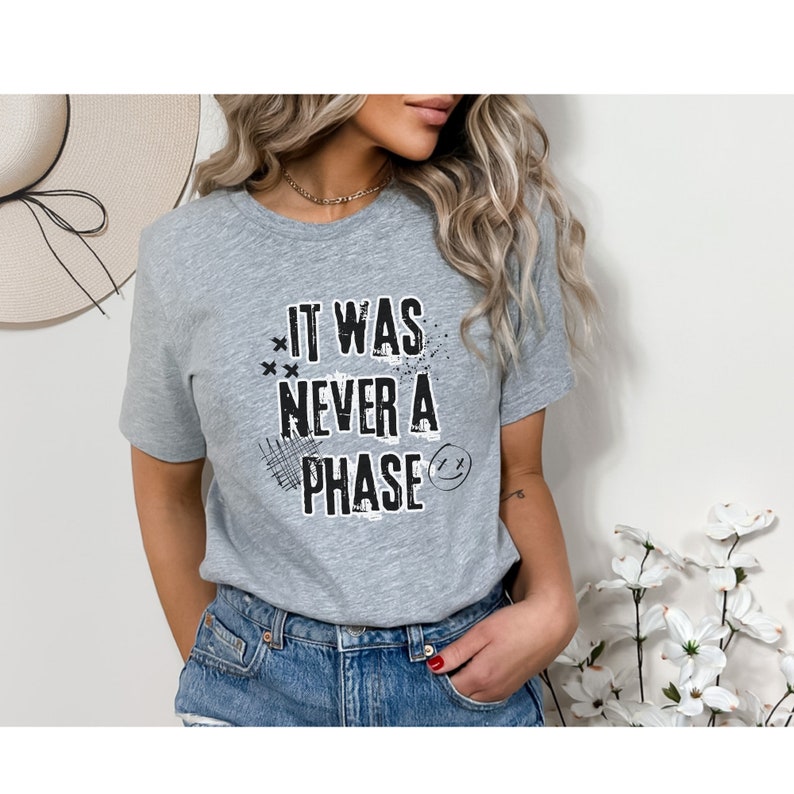 Może przedstawiać: Szary T-shirt z nadrukiem "It was never a phase" w kolorze czarnym, ze stylizowaną buźką i innymi elementami graficznymi.