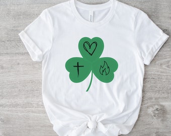 May include: White t-shirt with a green shamrock design. The shamrock has a heart, a cross, and a flame inside.