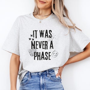 Może przedstawiać: Szary T-shirt z napisem "It was never a phase" w kolorze czarnym w stylu graficznym z efektem zużycia.