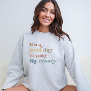 May include: A gray sweatshirt with the text "It's a good day to pray the rosary." printed in rainbow colors.