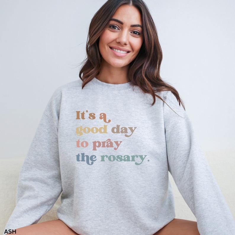 May include: A gray sweatshirt with the text "It's a good day to pray the rosary." printed in rainbow colors.