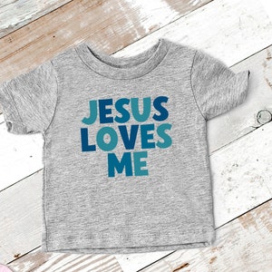 May include: A gray short-sleeved t-shirt with the words "JESUS LOVES ME" printed in blue and teal letters.