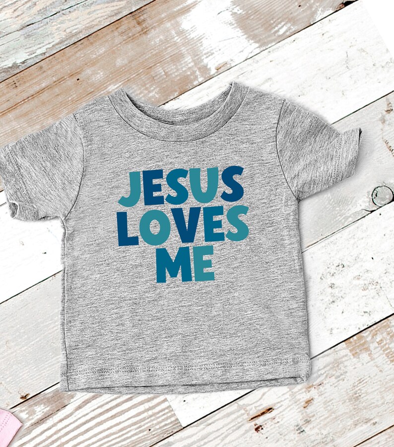 May include: A gray short-sleeved t-shirt with the words "JESUS LOVES ME" printed in blue and teal letters.