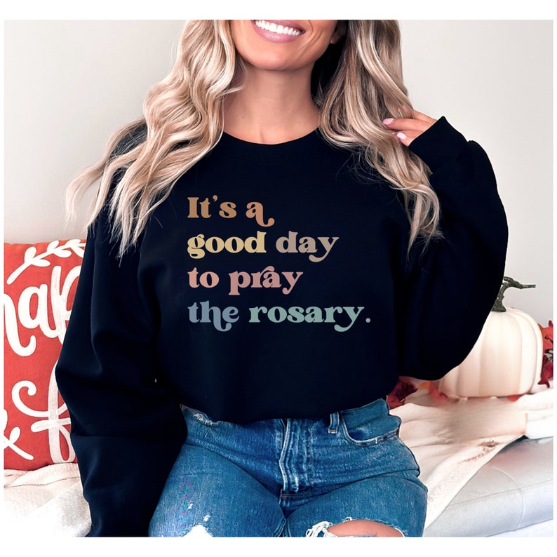 May include: Black sweatshirt with the text "It's a good day to pray the rosary." in rainbow colors.
